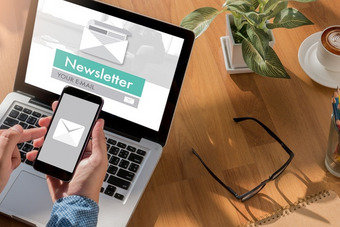 Laptop und Smartphone mit Newsletter-Anmeldung auf Schreibtisch neben Brille, Pflanze und Kaffee.