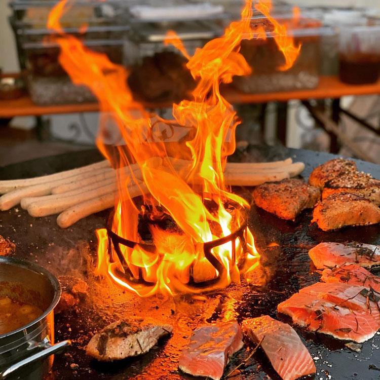 Offenes Feuer auf Grillplatte mit W&uuml;rstchen, Fleisch und Lachsfilets in Zubereitung