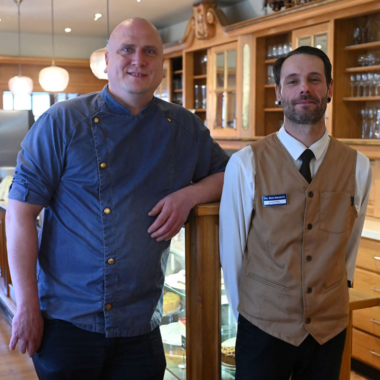 Alexander Schuhmacher und Frank F&ouml;rster stehen vor einer Holztheke mit Gl&auml;sern und Vitrine im Restaurant