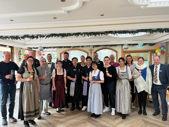 Gruppe in Trachten und festlicher Kleidung bei einer Feier mit Getr&auml;nken und Luftballons.