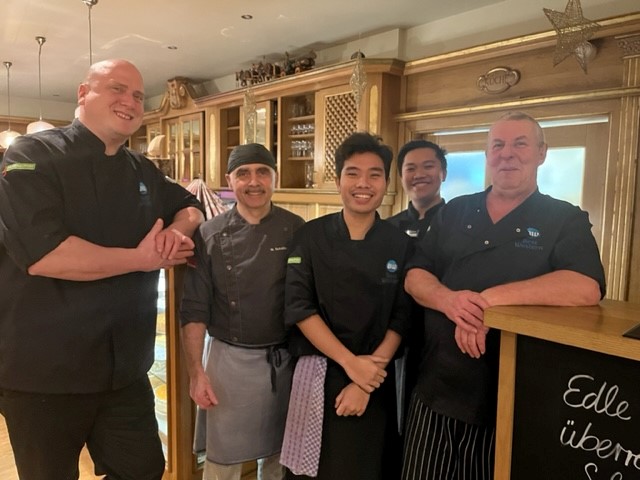 Gruppe von K&uuml;chenpersonal in schwarzer Berufskleidung steht vor einer Theke in einem Restaurant.
