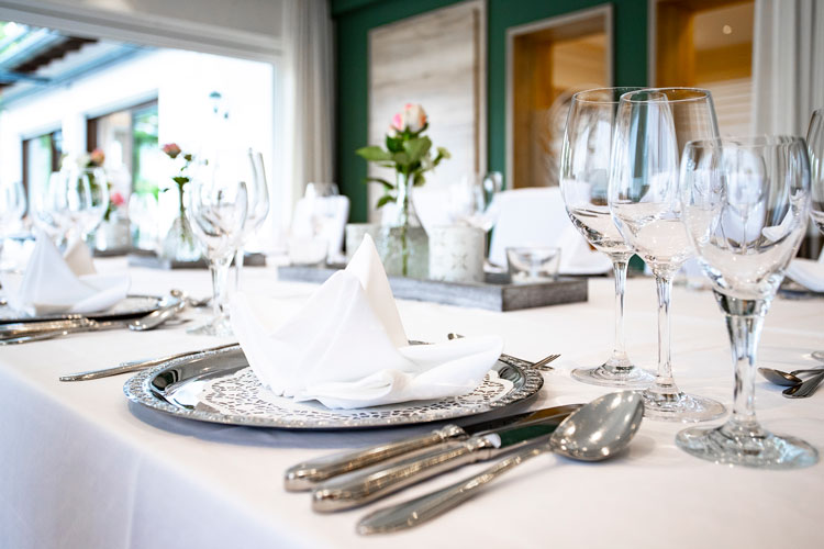 Festlich gedeckter Tisch mit wei&szlig;en Servietten, Besteck und Gl&auml;sern auf eleganter Tischdecke