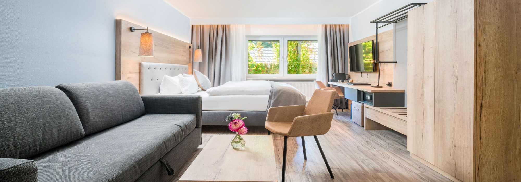 Modernes Hotelzimmer mit Doppelbett, Sofa, Schreibtisch und großem Fenster