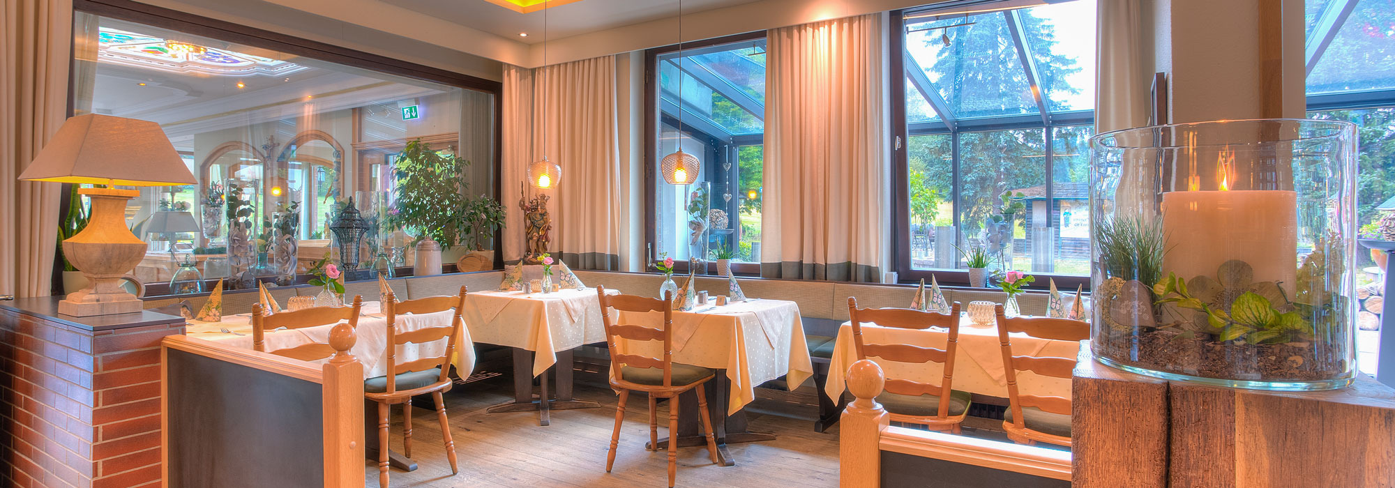 Helles Restaurant mit großen Fenstern, Holzdecke und festlich gedeckten Tischen