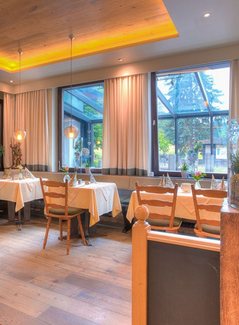Helles Restaurant mit großen Fenstern, Holzdecke und festlich gedeckten Tischen