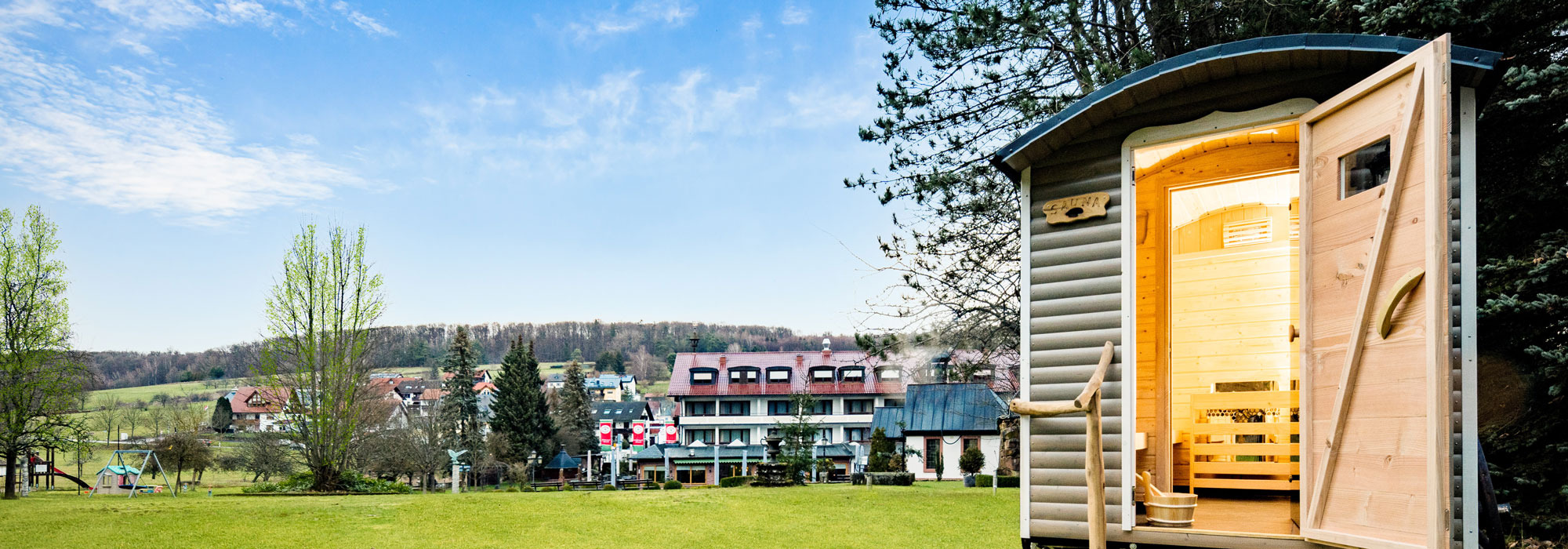 Freistehende Außensauna mit Holzinterieur auf grüner Wiese vor Hotelanlage