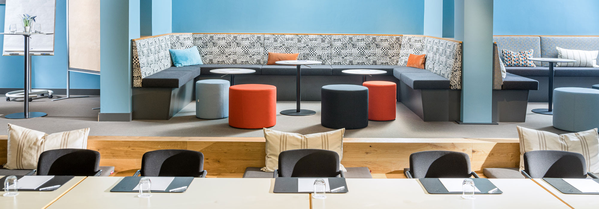 Moderner Seminarraum mit blauen Wänden, gepolsterter Sitzecke, Hockern und Tischen für Gruppenarbeit