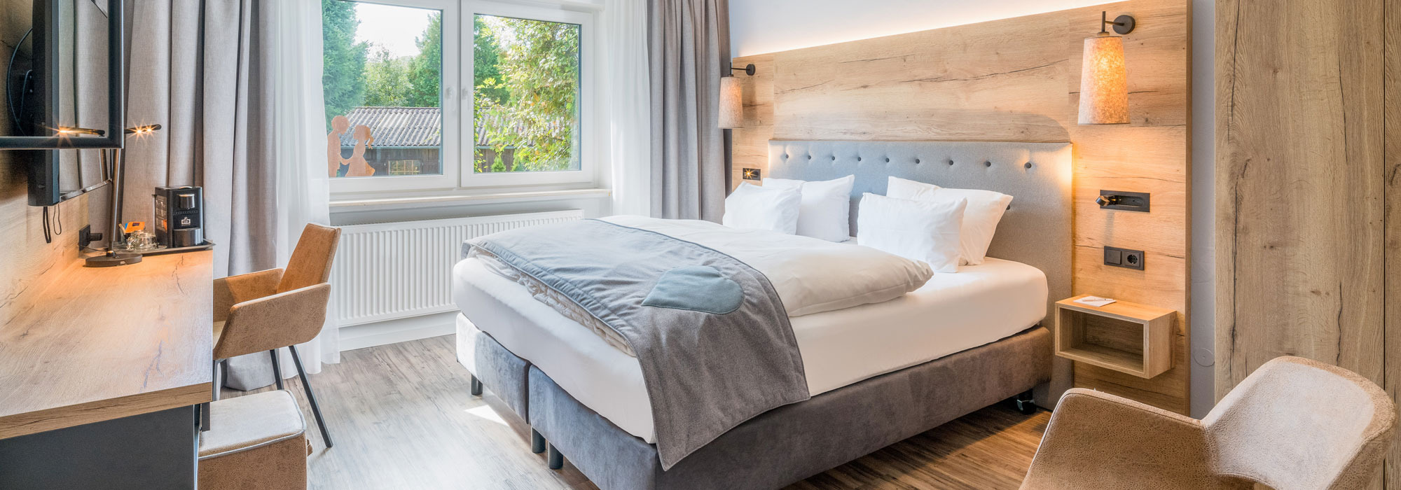 Modernes Hotelzimmer mit Doppelbett, Schreibtisch und großem Fenster