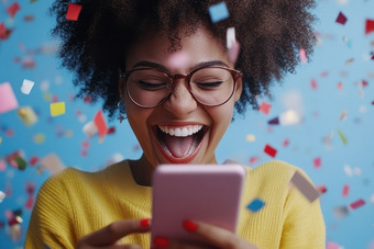 Person hält ein Smartphone vor blauem Hintergrund mit buntem Konfetti in der Luft, trägt gelben Pullover